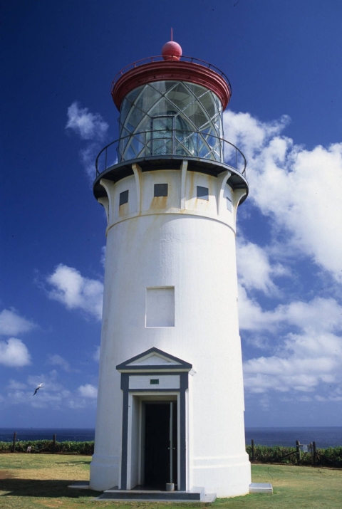 A close-up view of a tall white lighthouse with a door at its base and a red roof atop its light