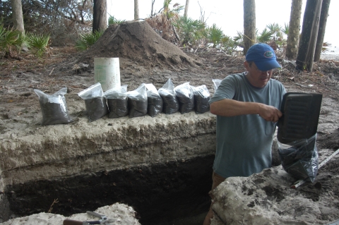 A man standing in an excavated hole and bagging soil samples from an archaeological dig