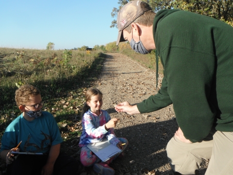 An adult holds a banded songbird for a student to touch while another student watches