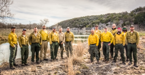 A group of 14 in yellow shirts and khaki pants and caps looks at camera.