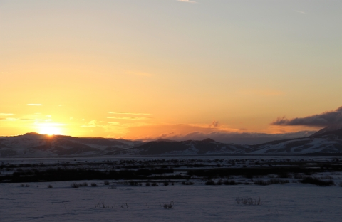 An orange and yellow mountain sunrise over a snowy valley