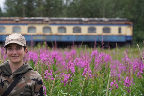 woman standing in front of a train with fireweed