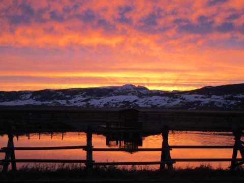 Sunrise of bright orange and yellow over mountains and a pond. 