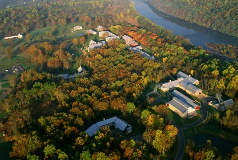 Ariel of fall trees with multiple building with river flowing behind in background
