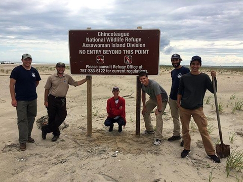 Five people pose for a picture next to a sign that reads Chicoteague National Wildlife Refuge Assawoman Island Division 