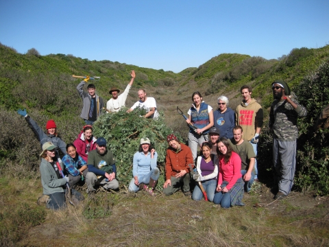 Smiling group of volunteers next to a pile of non-native plants that they removed