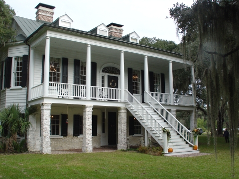 Angled front view of the Grove Plantation Manor. Two pumpkins are on the bottom step and plants are on the bottom of the hand railings. 