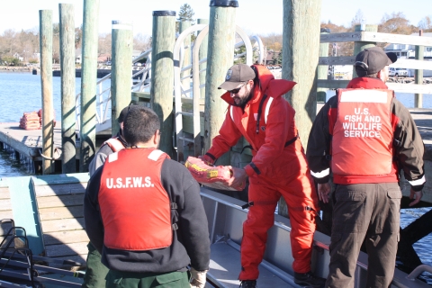 Three people-- two in orange USFWS vests-- load a boat with supplies.