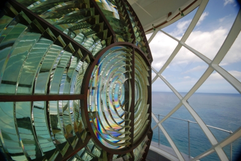 A closeup of a lighthouse lamp with the ocean visible in the background