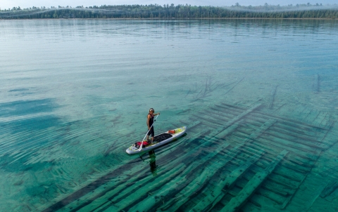 A paddle boarder on an aqua blue body of water with forested land in the distance