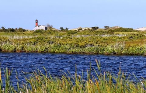 A distant view of a red-towered lighthouse next to water