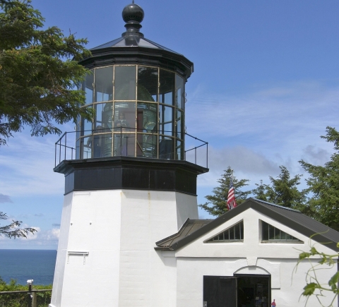 A short white lighthouse with a large light in a black-and-glass enclosure
