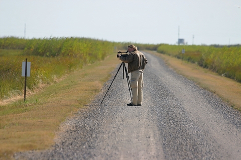 A M\man on a gravel road bird watching with a scope on a tripod