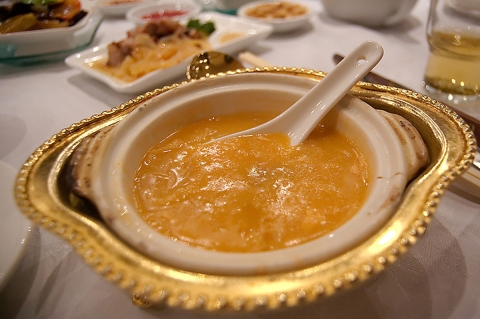 A bowl of shark fin soup in a Chinese bowl on a table of other food. 
