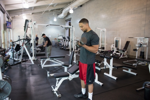 man standing with weight in exercise room full of equipment