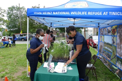 Neighborhood member approaches John Heinz NWR booth as Service staff engages with her.