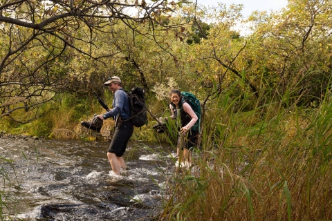 Two people cross an ice-cold creek at Kodiak National Wildlife Refuge in Alaska.