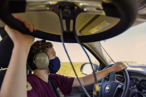 an Intern wearing headphones holds a tracking wheel as she drives and listens for radio signals.