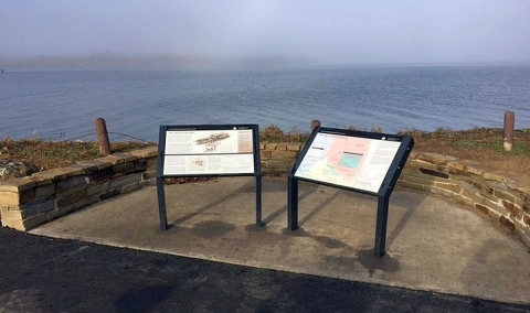 Two panel displays with indistinguishable words and image next to a blue river in a foggy setting