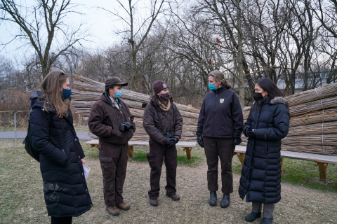 5 people in winter clothing stand together on a refuge. Two wooden benches are behind them