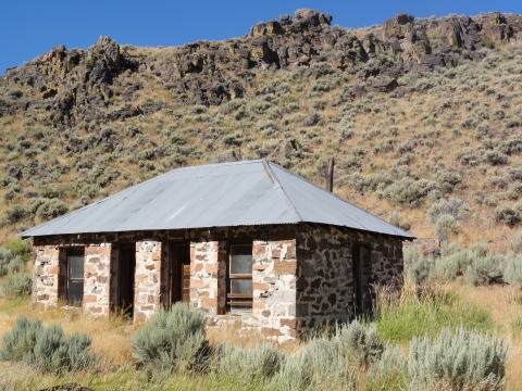 Historic brick building with metal roof in sagebrush habitat with rocky outcropping in background