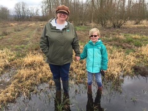 Woman and child hold hands, standing in a muddy puddle in a field during wintertime. 