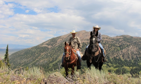 Two horseback riders in the mountains pose for a picture.