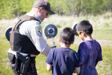 A uniformed Refuge System law enforcement officer helps two children at target practice.