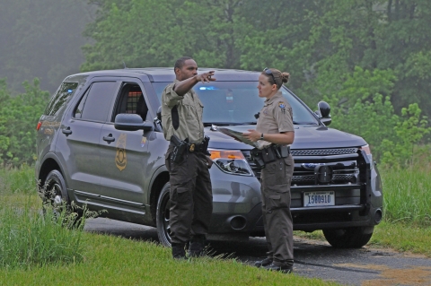 Two uniformed Refuge System law enforcement officers talk by a police vehicle and one points.
