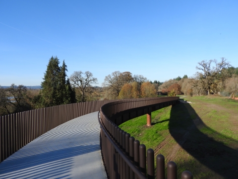 A paved pedestrian bridge leads away from the viewer to high ground on the other side.