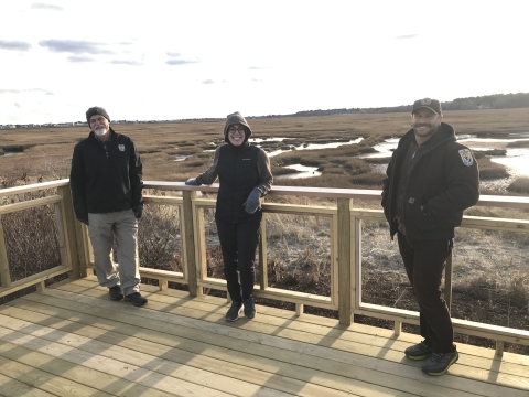 Three USFWS staff stand on an observation deck overlooking the saltmarsh on the Webhannet River in Maine.