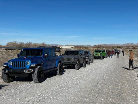 Group of Jeeps lined up along a dirt road while people mill around