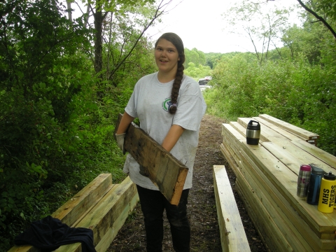 A youth conservation corps (YCC) member carries a wooden beam to construct a new bridge along a refuge trail.