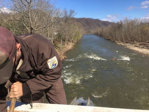 A USFWS employee leans over the tank of a fish stocking truck. Behind him is the green, fast-flowing Nolichucky River 
