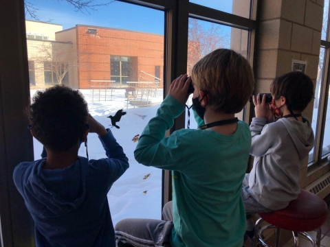 Children use binoculars at a window