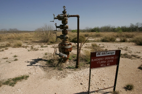 A rusting gas well stands in a patch of dirt.