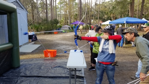 Volunteer gives instruction to a young lady in archery at the St. Marks National Wildlife Refuge as part of the Wildlife, Heritage, and Outdoor Festival. The arrows are foam tipped to prevent serious injury. This image captures the arrow in mid-flight.