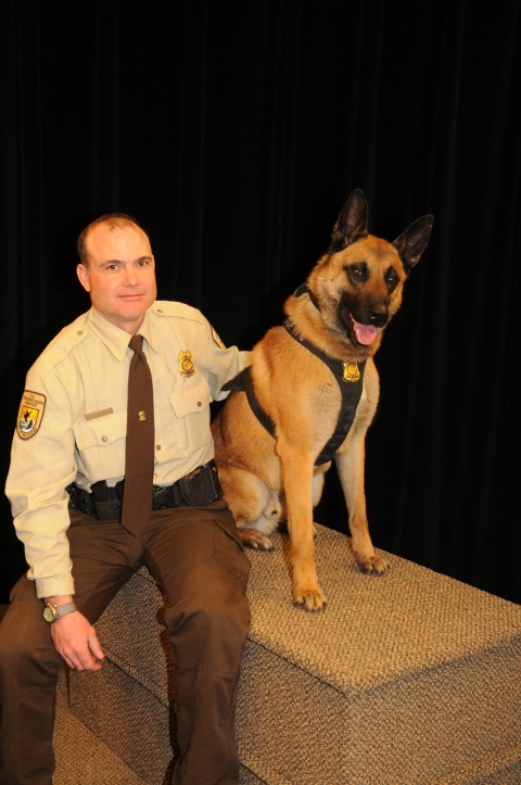 man in USFWS uniform sits on platform next to dog