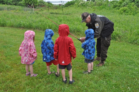 Image of a USFWS staff member showing four children a fishing pole