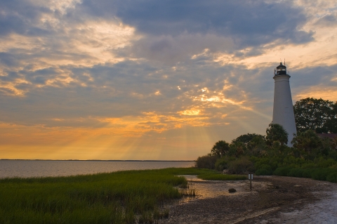 The Historic St. Marks Lighthouse with a backdrop of a beautiful orange and blue sunset over Apalachee Bay.