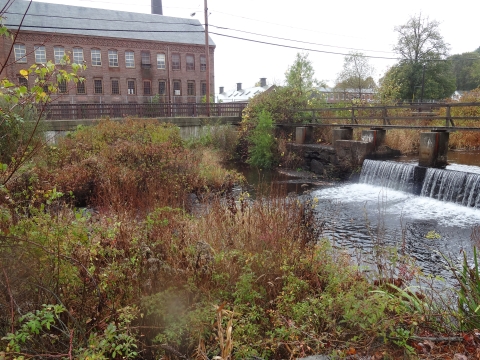 water flows over dam next to brick building