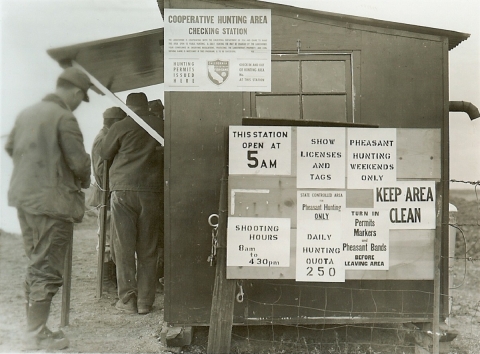 sac check station circa 1955 with 4 hunters in frame and various signs