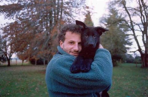 A man with dark, curly hair wearing a blue fleece and holding his dog, a black lab puppy
