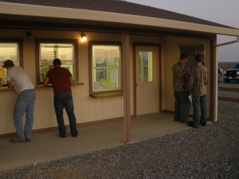 image of front of hunter check station with two hunters talking to staff at windows. two other hunters looking at map