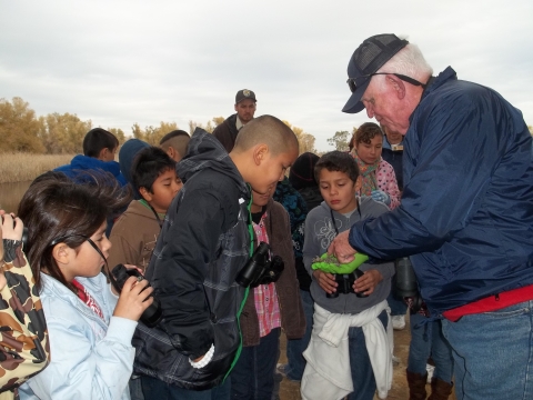 volunteer showing a group of kids remains of an owl pellet. group of about 15 kids