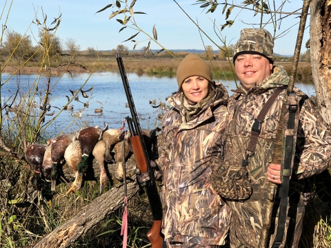 Two duck hunters holding shotguns pose with water in the background at Ridgefield National Wildlife Refuge