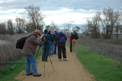group of about 10 people on trail. person in foreground has a spotting scope out looking for owls
