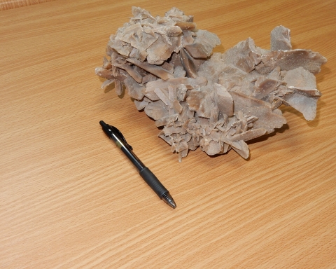 A crystal formation lies next to a pen for size comparison. The crystals are several times larger than the pen.