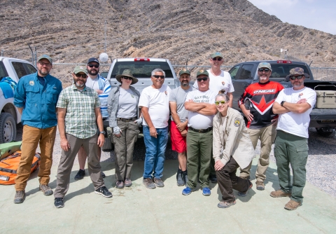 A group of eleven people standing in front of pickup trucks and smile at the camera