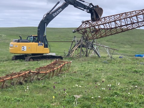 An excavating machine plucks a rusted tower up from a field.